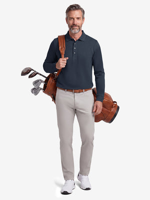 Front full body shot of model wearing navy solid stretch cotton pique long sleeve polo shirt while carrying a golf bag on back