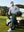 Model in olive green stretch plain everyday pants leaning against a golf cart, full-body shot