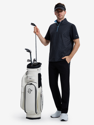 Front full body shot of model wearing navy flower full print quarter zip sleeveless vest pullover with a golf club in hand and golf bag beside
