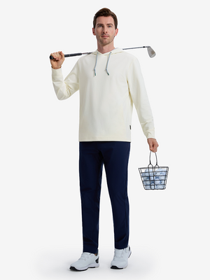 Front full body shot of model wearing cream soft stretchy hoodie with inner print hood, carrying a golf club on shoulder with one hand and holding a basket of golf balls in the other hand